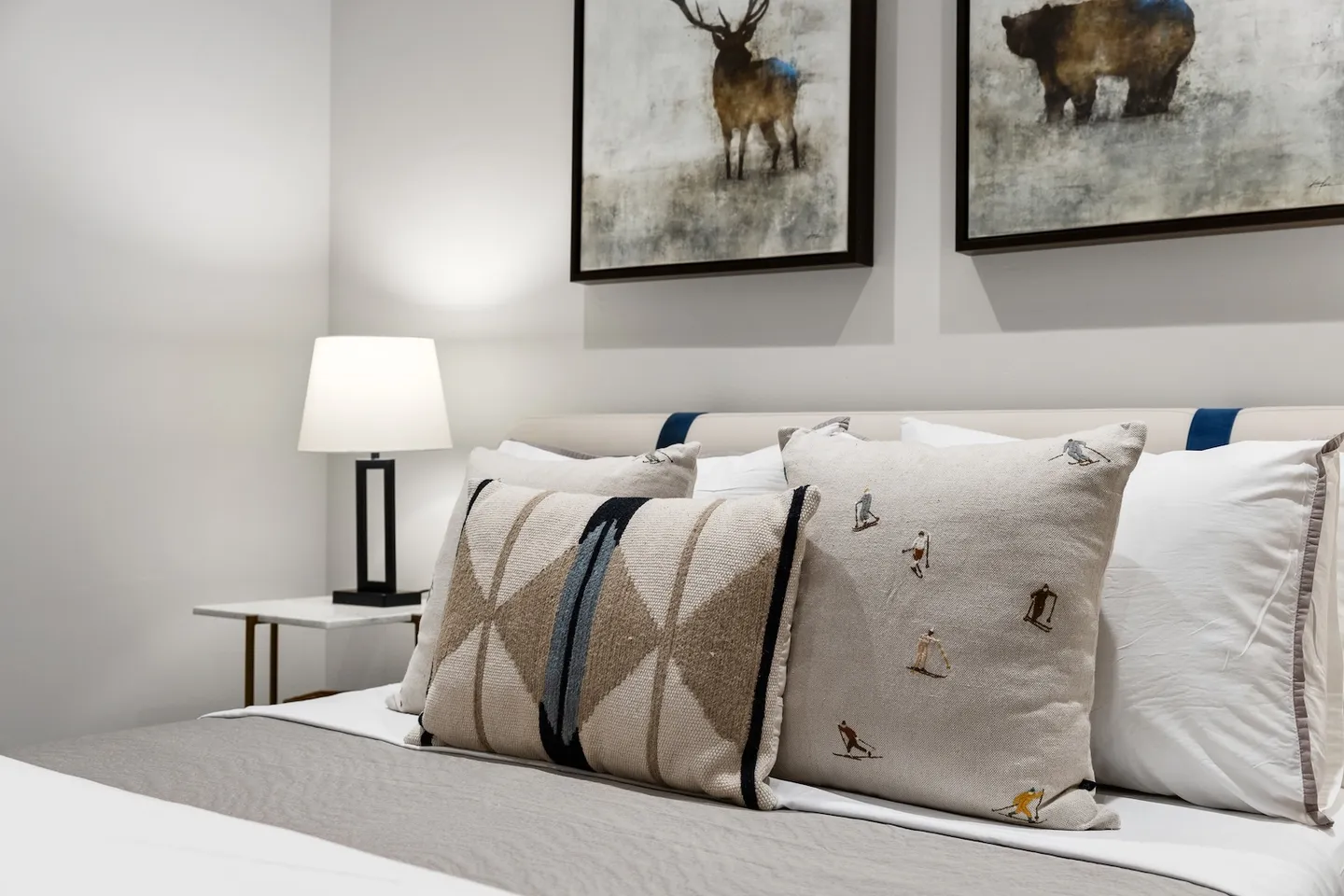 Close-up of a neatly made bed with decorative pillows, an illuminated bedside lamp, and framed wildlife art on the wall.
