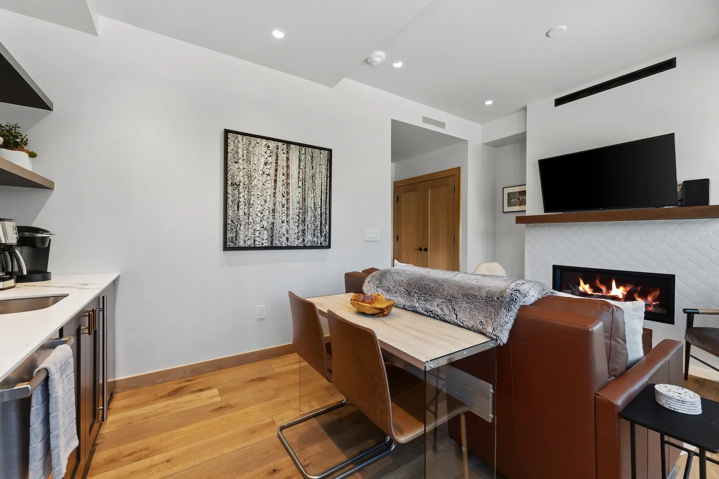 Open-concept living and dining area featuring a table with chairs, a leather sofa, and a wall-mounted fireplace beneath a television.