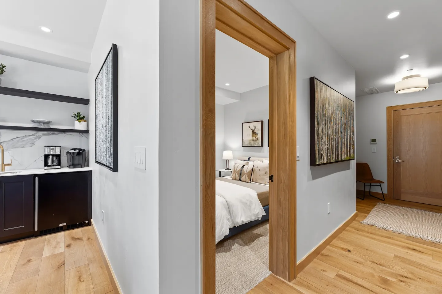 Hallway with wood-trimmed doorway leading to a bedroom, adjacent to a small wet bar and an entry area.