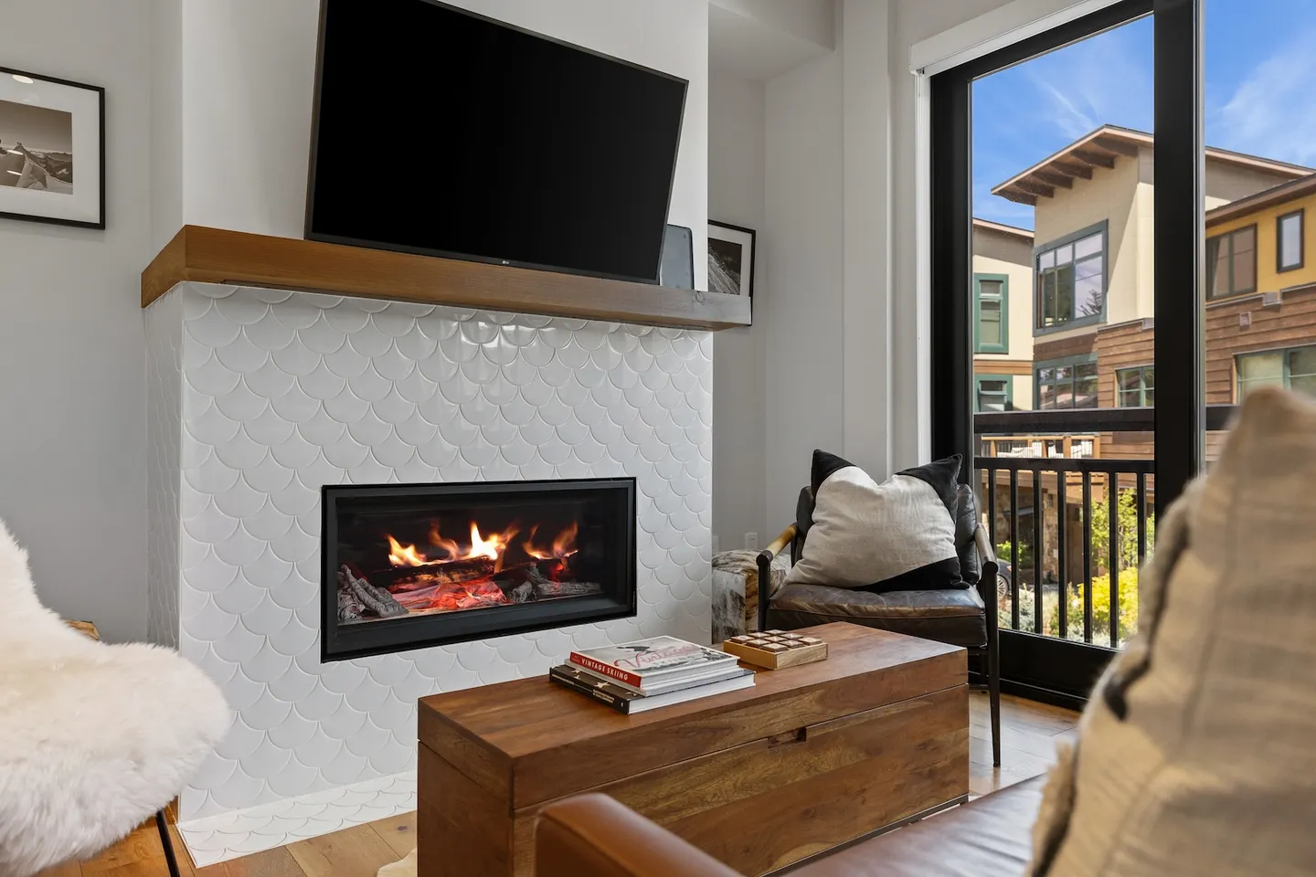 Living area featuring a fireplace with white scalloped tile, a wall-mounted TV, wooden coffee table, and an adjacent glass door.