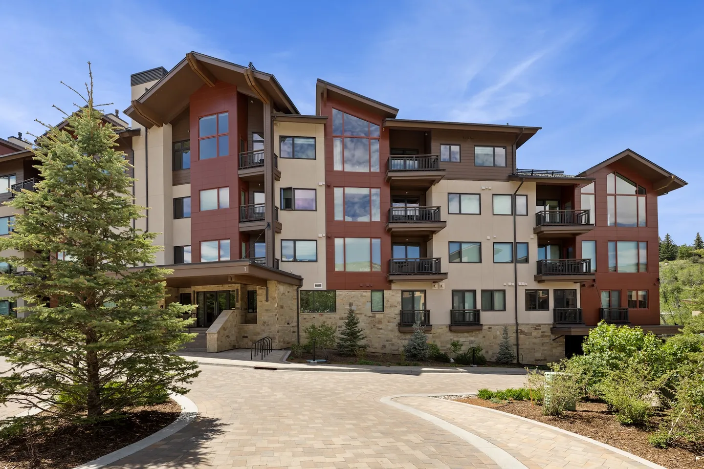 Exterior view of a multi-story modern lodge building featuring stone accents, dark red and beige siding, balconies, and a paved circular driveway.