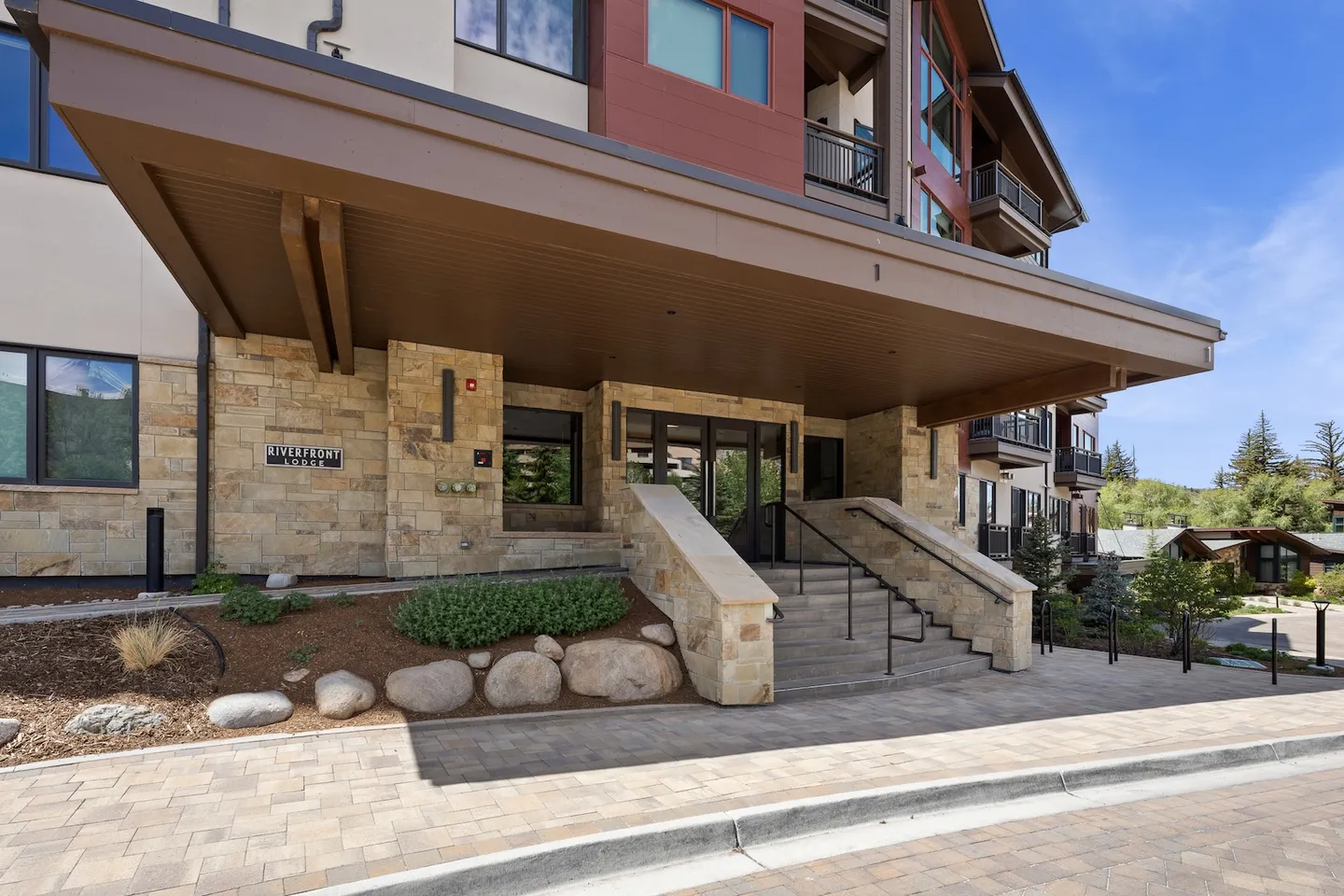 Exterior entrance of Riverfront Lodge featuring stone facade, covered portico, and steps leading to double glass doors.