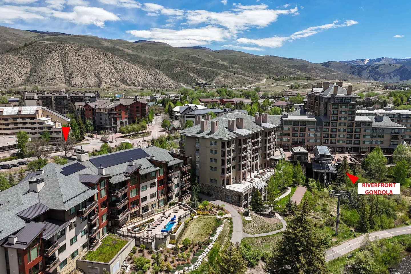 Aerial view of a mountain resort complex showing multiple lodge buildings, an outdoor pool, walking trails, and a gondola lift with surrounding hills.