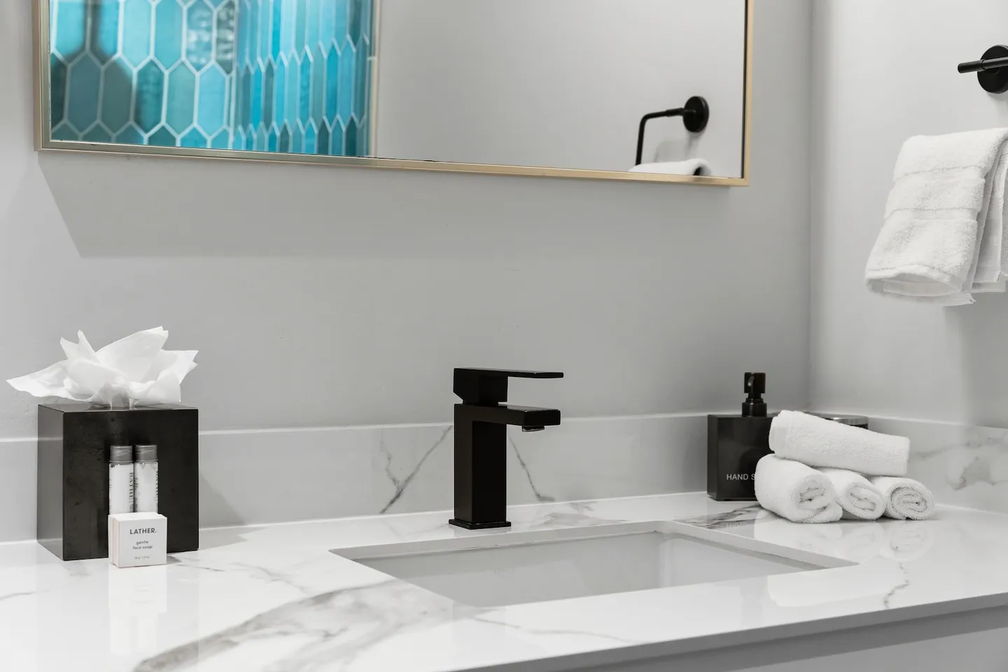 Bathroom vanity with a white marbled countertop, undermount sink, matte black faucet, and mirror reflecting bright blue shower tile.