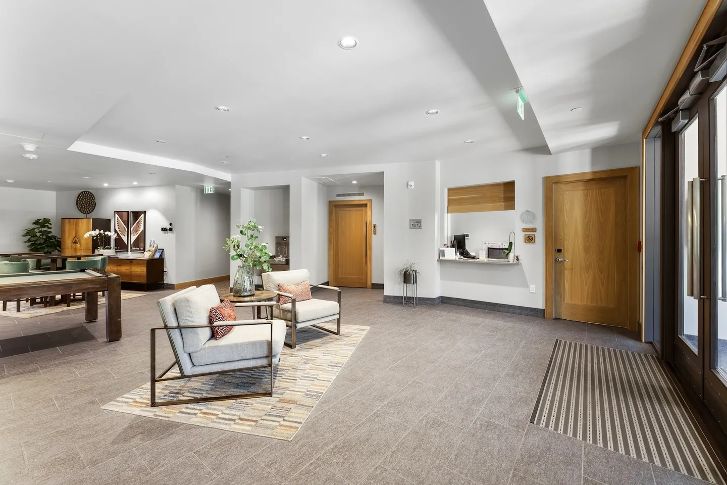 Spacious building lobby with tile flooring, a seating area, front desk counter, and a pool table visible in an adjacent room.