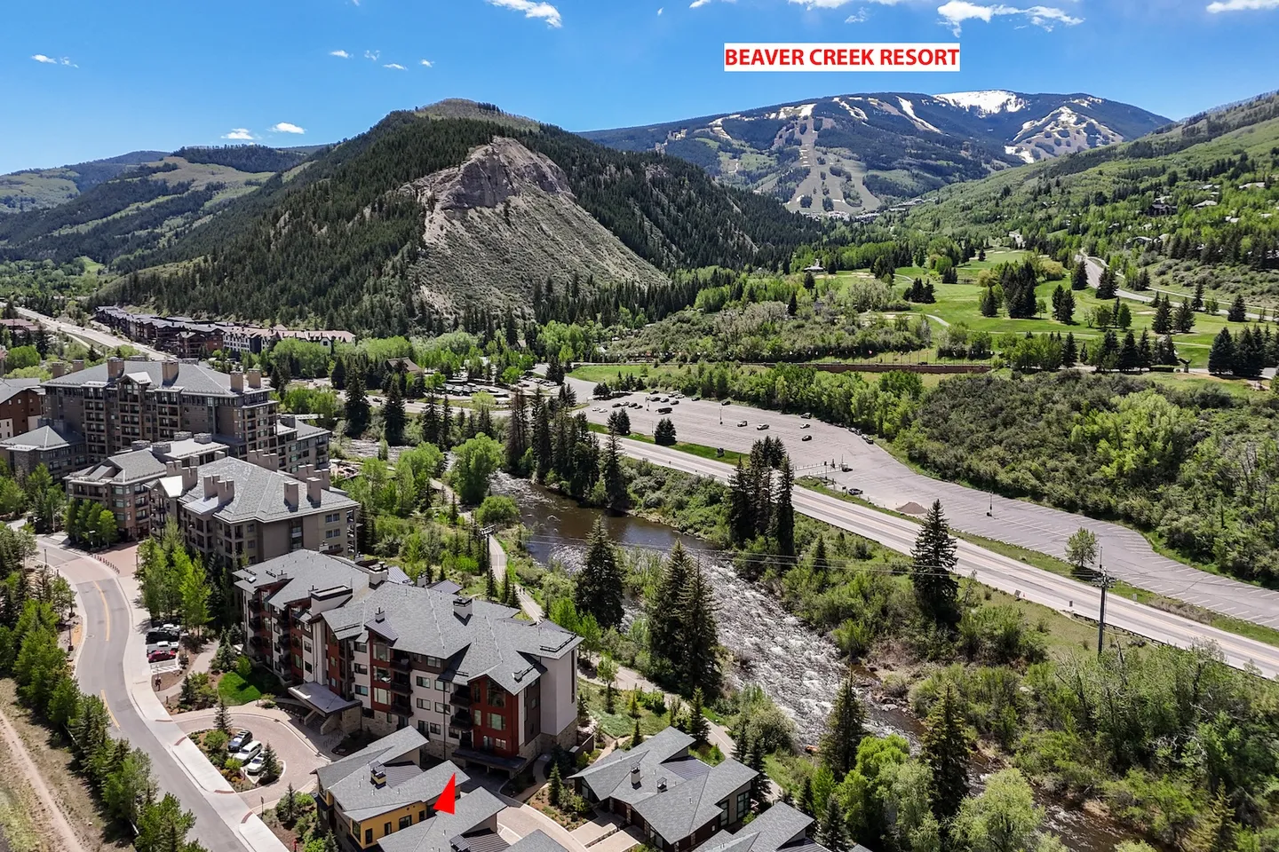 Aerial view of multi-story mountain condominium buildings along a river with ski slopes in the background.