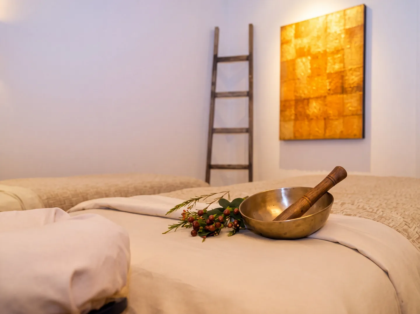 Massage table set with linens, a singing bowl, and decorative greenery in a spa room.