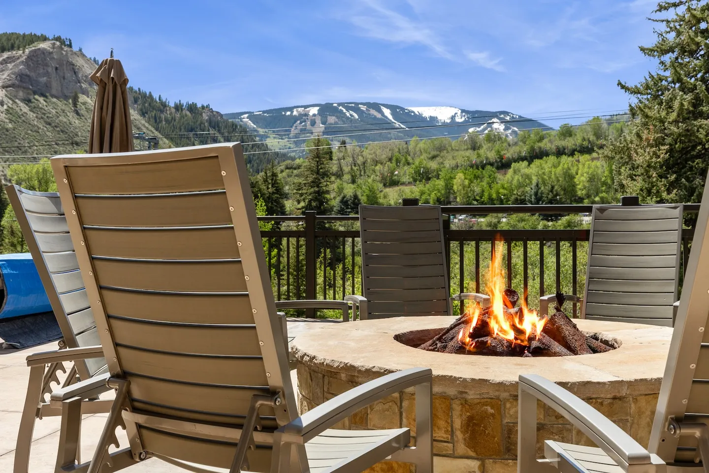 Outdoor patio with a stone fire pit, seating, and a view of mountains with snow patches under a clear sky.