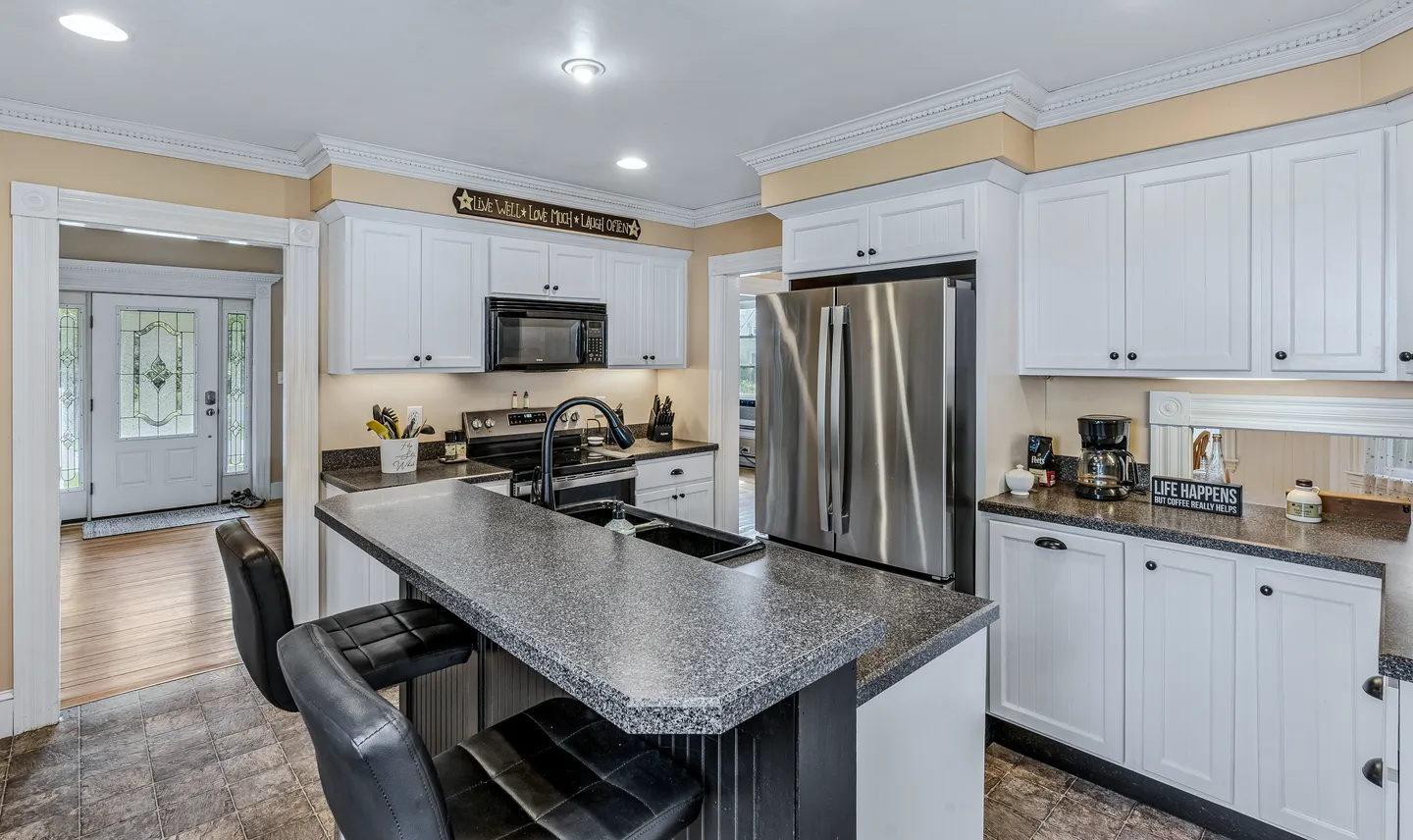 Kitchen with white cabinetry, dark speckled countertops, stainless steel appliances, and a breakfast bar with two black stools.