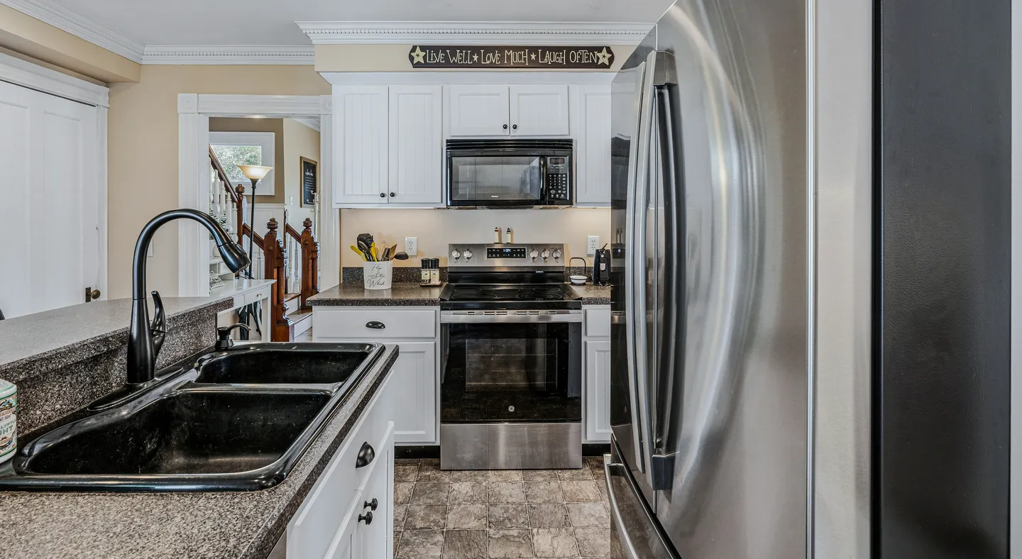 A kitchen with white cabinets, dark countertops, a double-basin black sink, and stainless steel appliances.