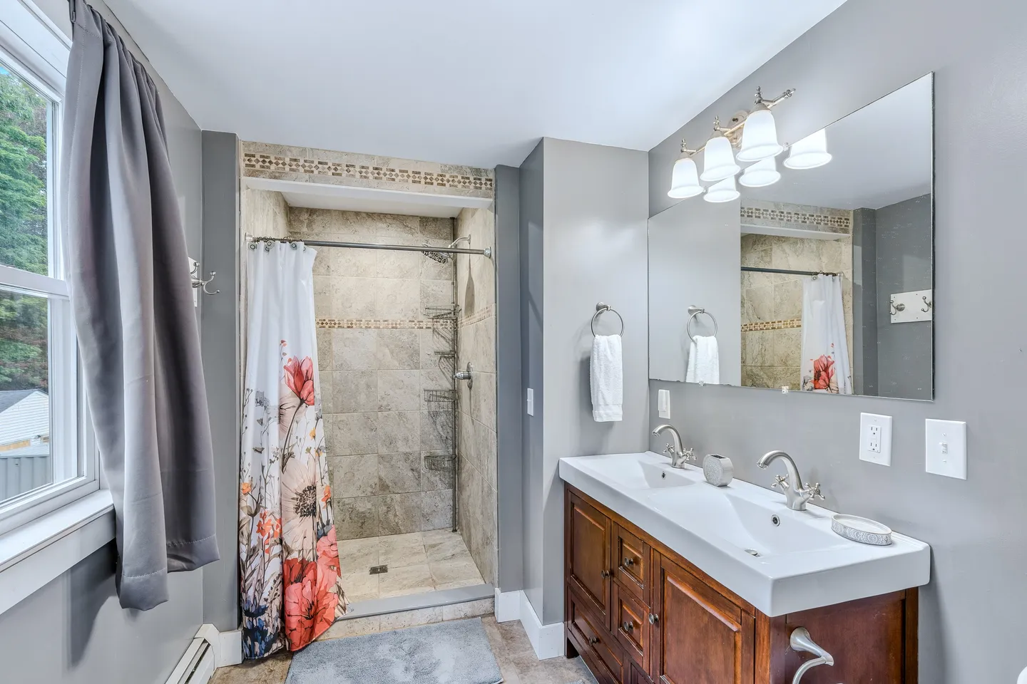 Bathroom with a double-sink wood vanity, large mirror, and tiled walk-in shower with a floral curtain.