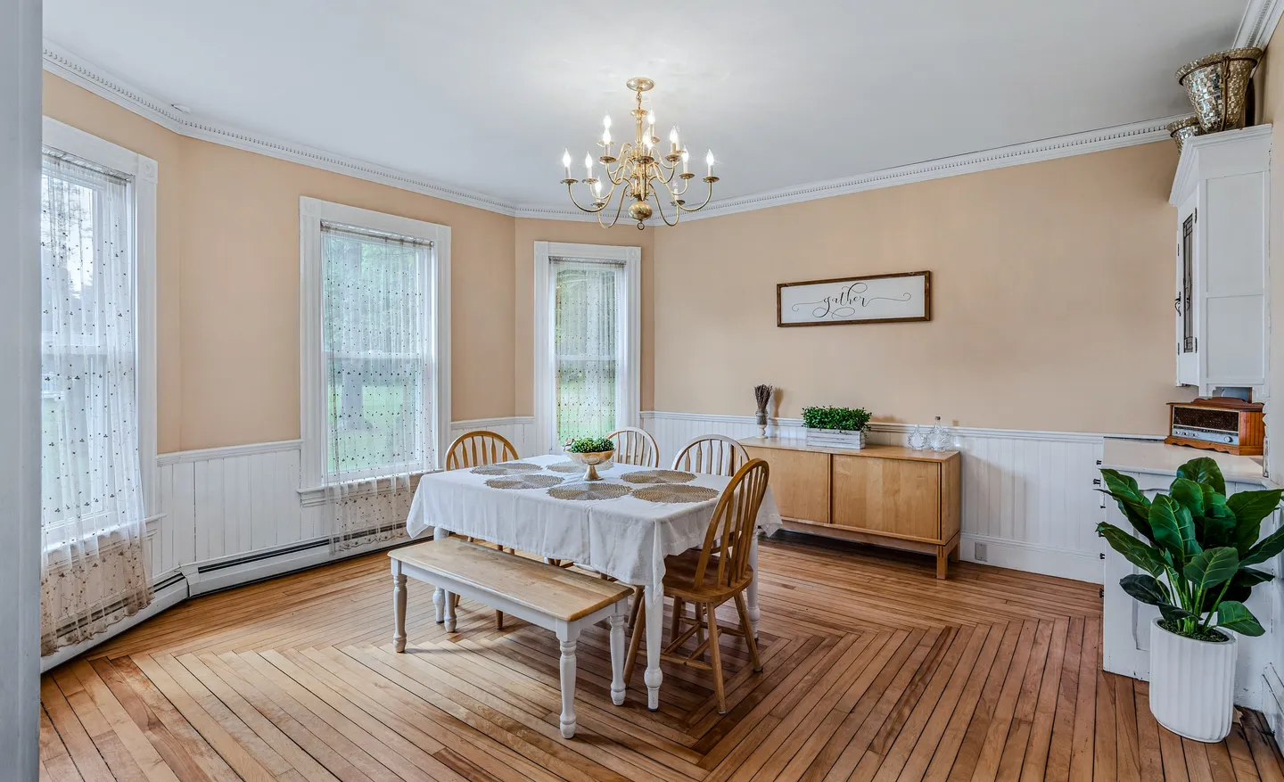 Dining room with wood flooring laid in a diamond pattern, a dining table with chairs and a bench, and a chandelier.