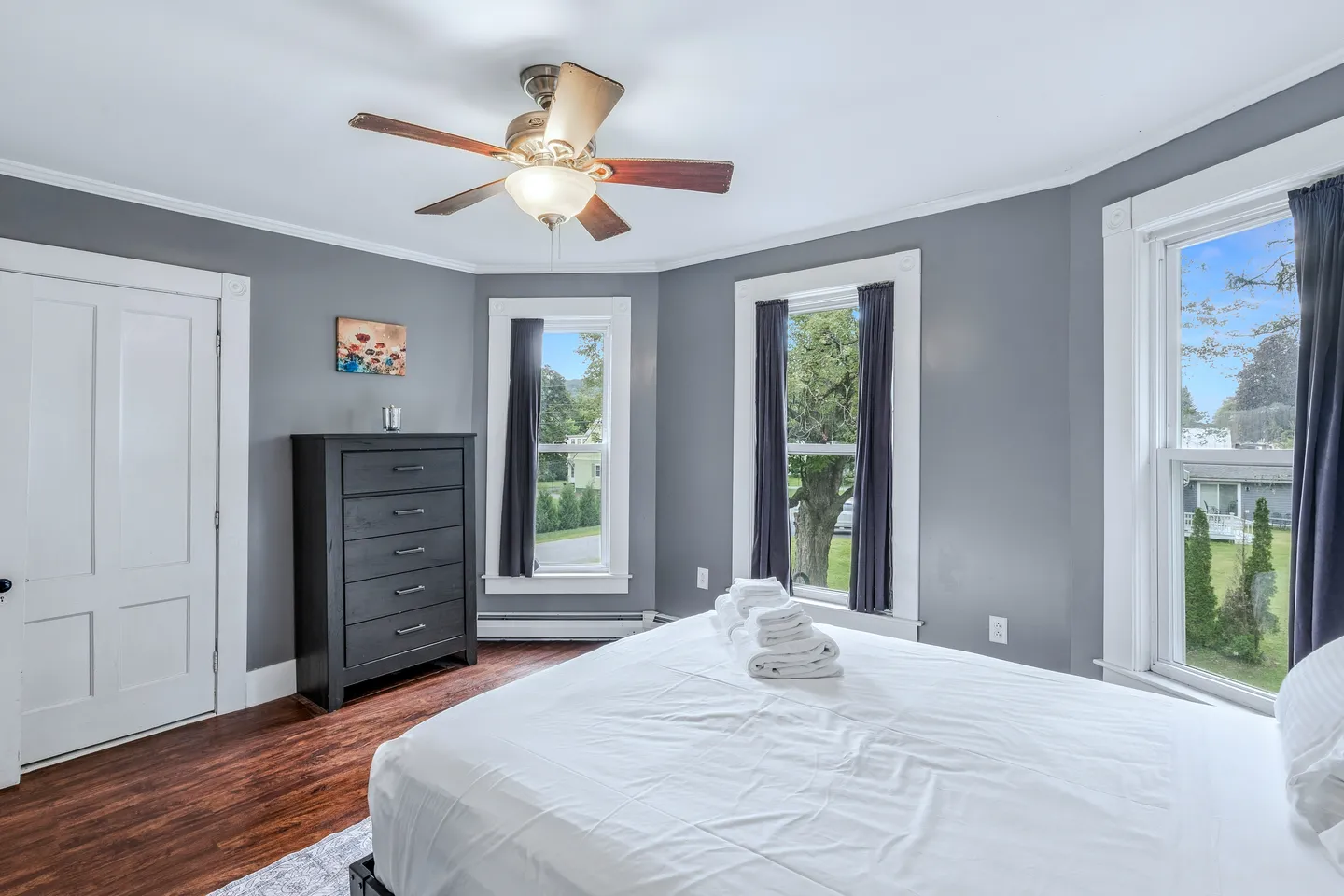 Bedroom with gray walls, wood flooring, a ceiling fan, black dresser, and a bed with white linens.