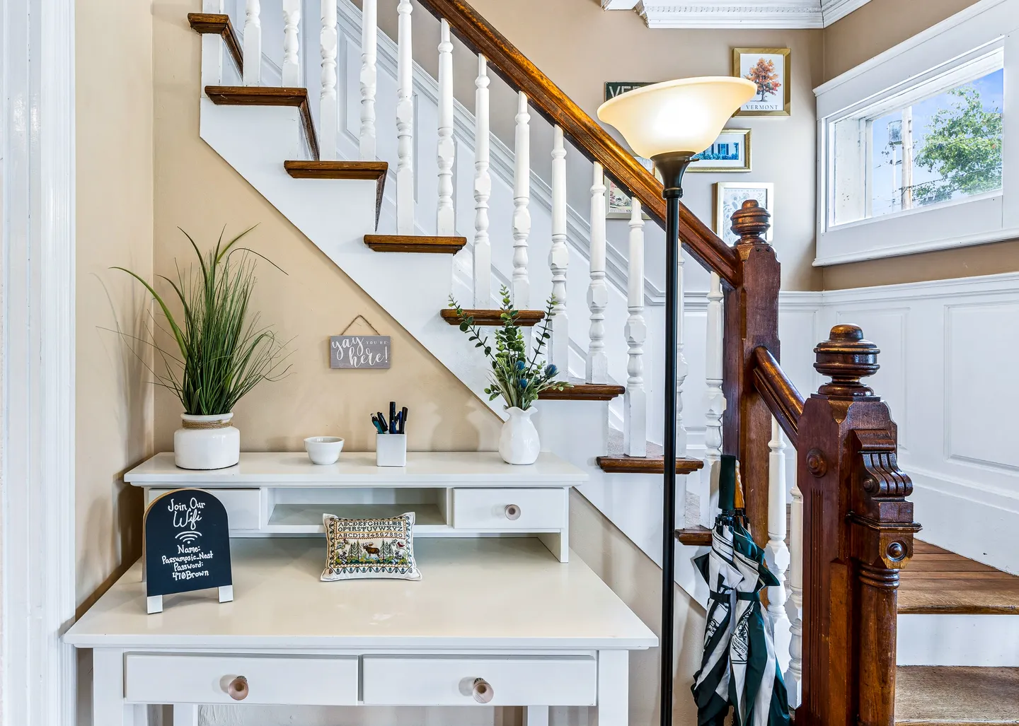 A white wooden desk with small drawers and decor tucked under a wooden staircase with white spindles.