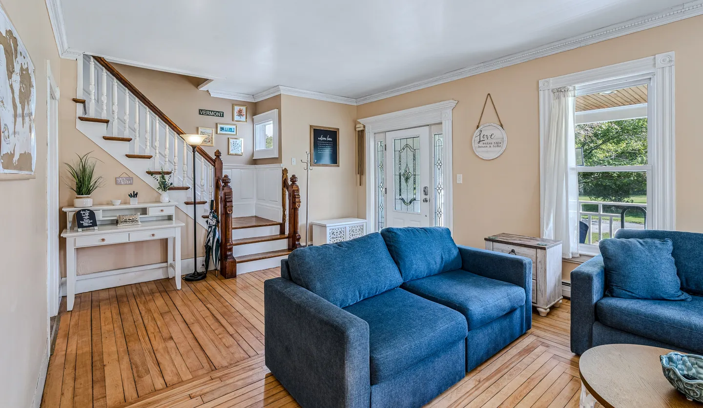Living room and entryway with blue sofas, hardwood floors, front door with glass inserts, and a wooden staircase.