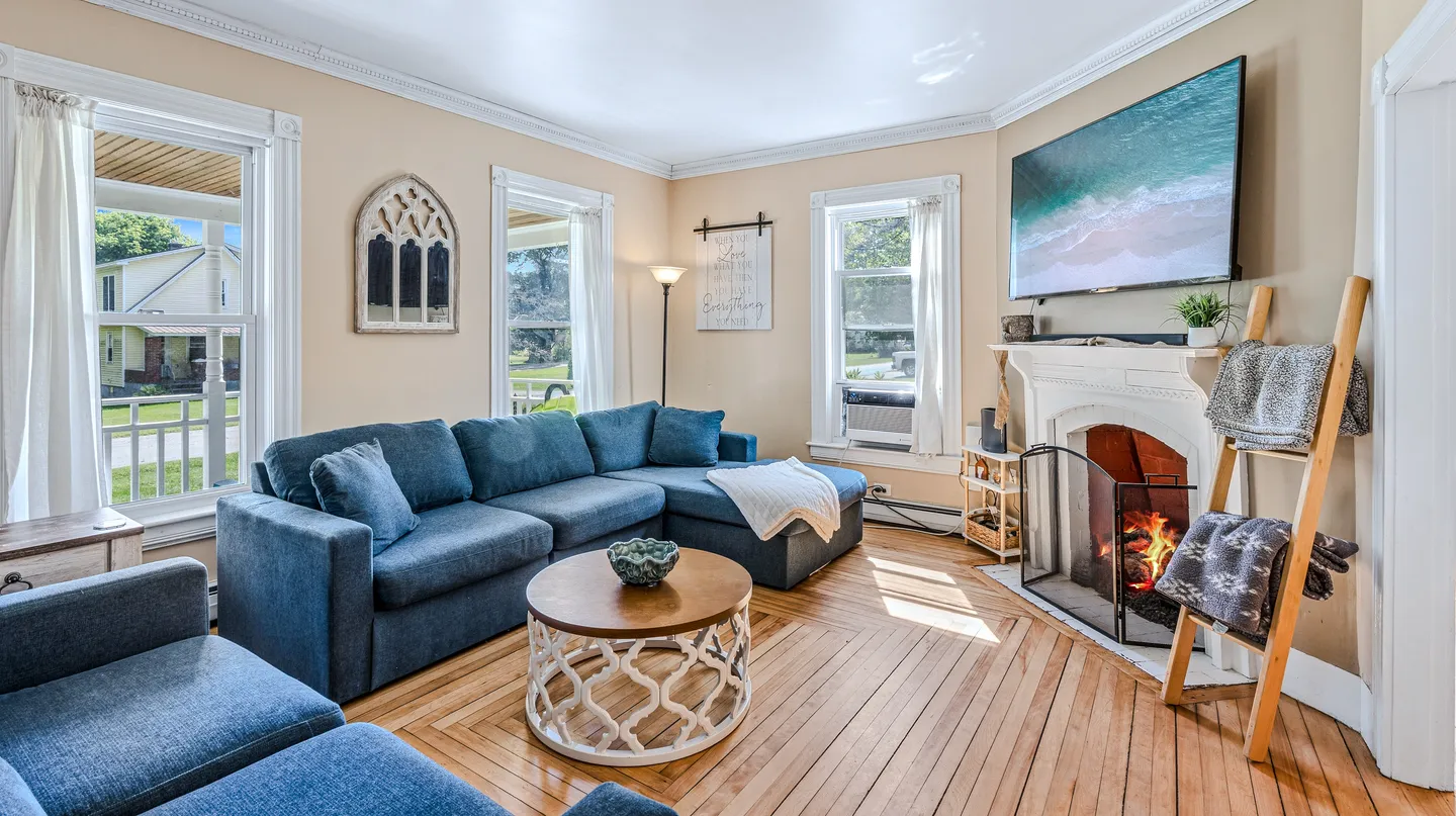 Living room with wood flooring, a blue sectional sofa, a round coffee table, and a wall-mounted TV above a fireplace.