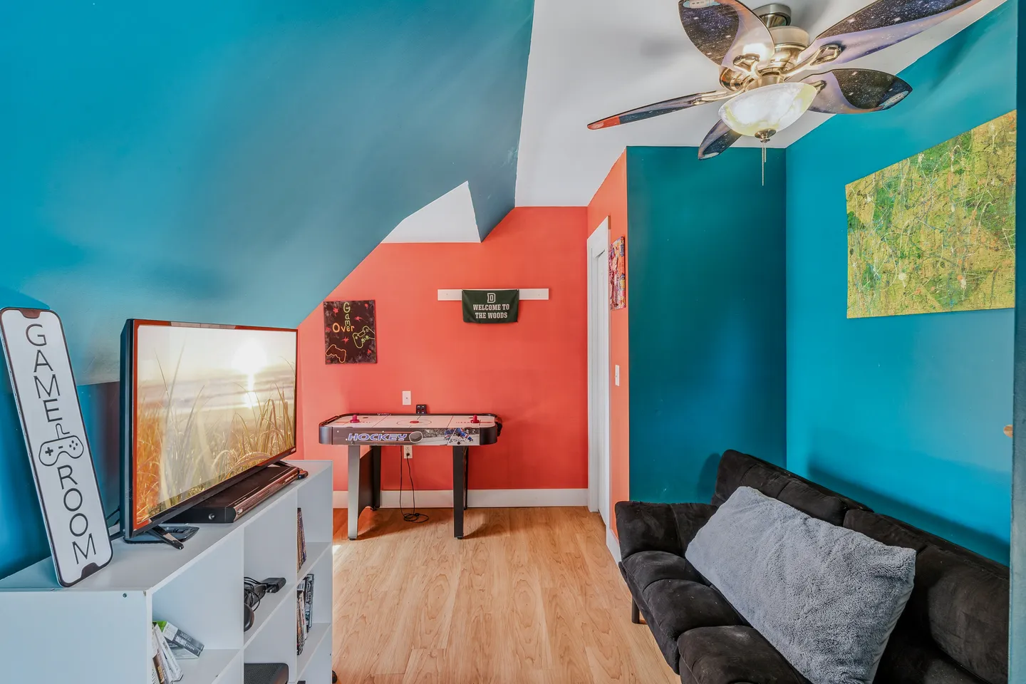 Game room with brightly painted blue and coral walls, an air hockey table, television on a white shelving unit, and a dark sofa.