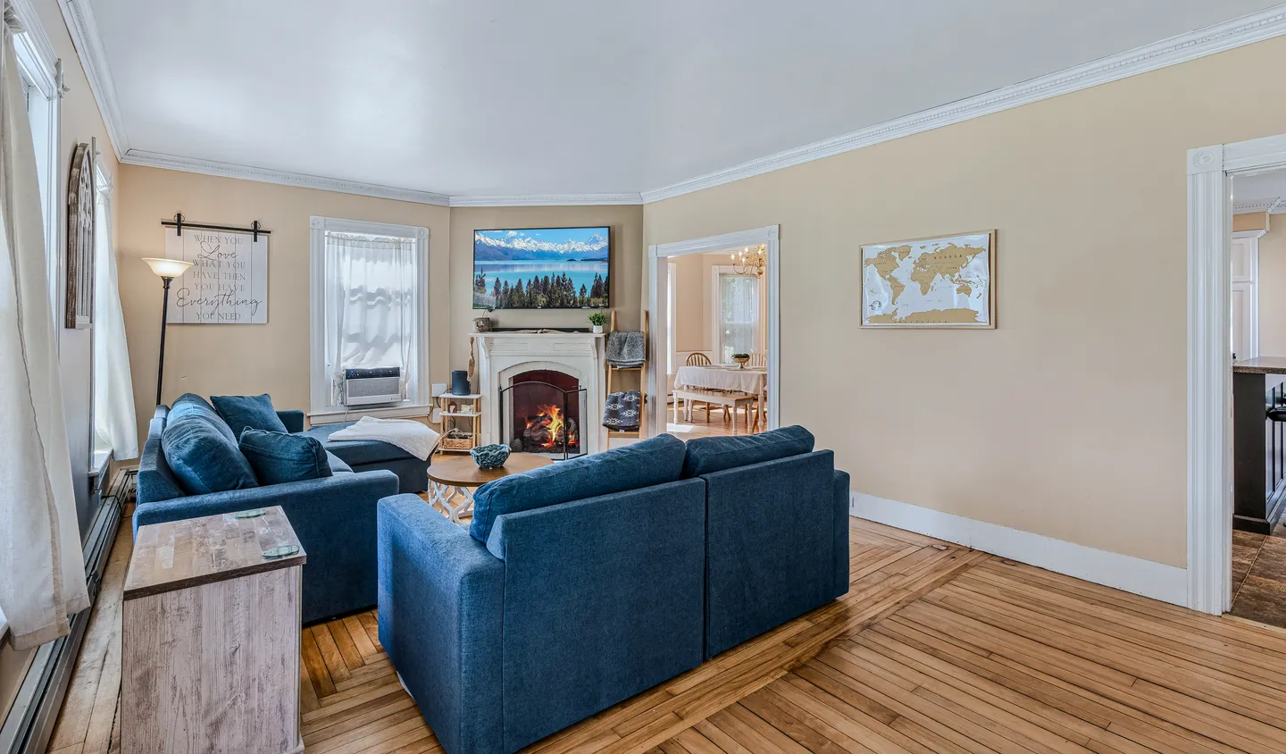 Living room with blue upholstered sofas, wood flooring, a fireplace, and a wall-mounted TV.