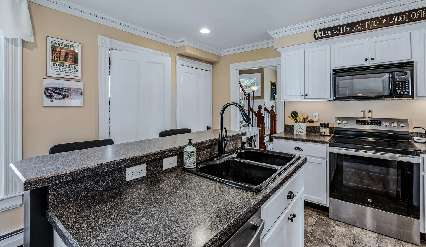 Kitchen featuring a multi-level breakfast bar counter with a black double sink, white cabinetry, and stainless steel appliances.