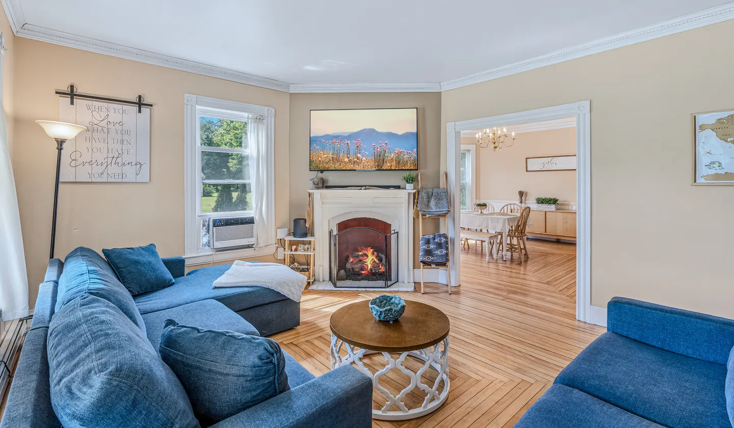 Living room with blue upholstered sofas, wood flooring, a fireplace with a mantel, and a wall-mounted TV.