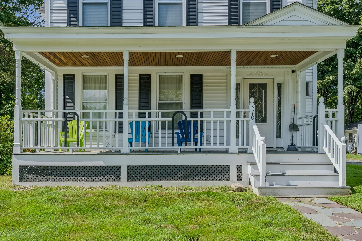 Front covered porch of a white house with steps, railings, and Adirondack chairs.