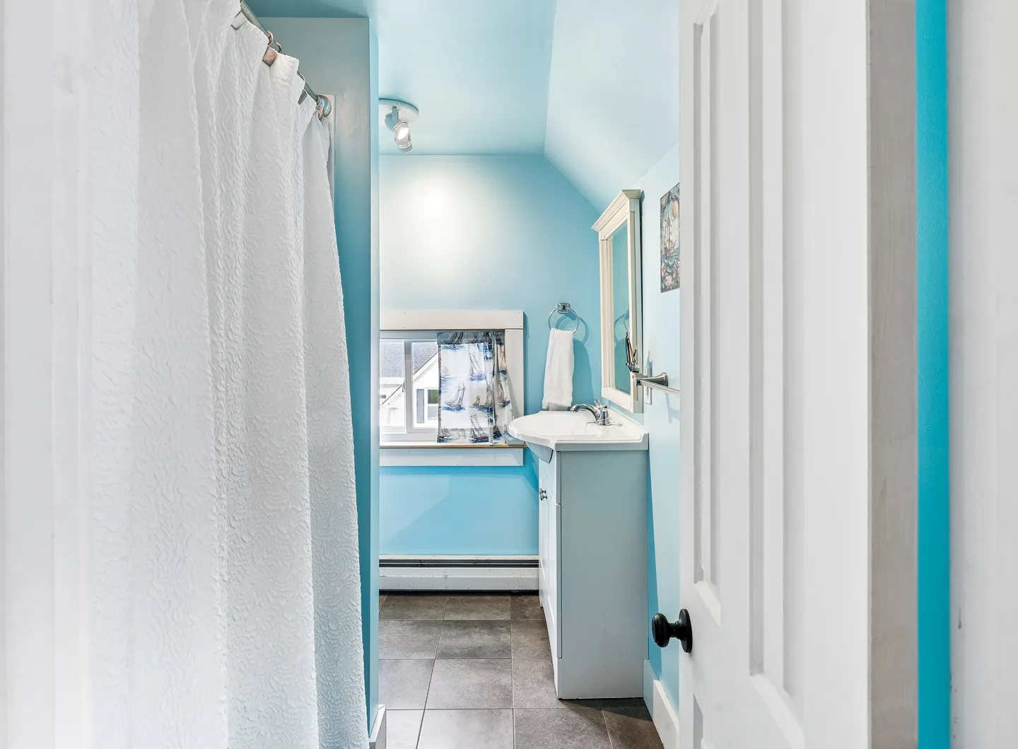 Bathroom with light blue walls, dark tiled floor, white vanity with mirror, and shower curtain.