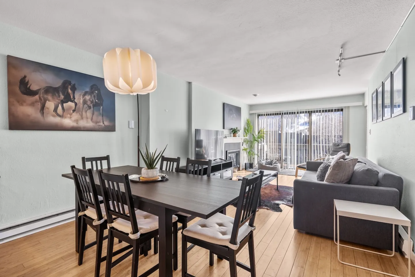Open-concept dining and living room with a dark wooden dining table, a grey sofa, and sliding glass doors leading outside.