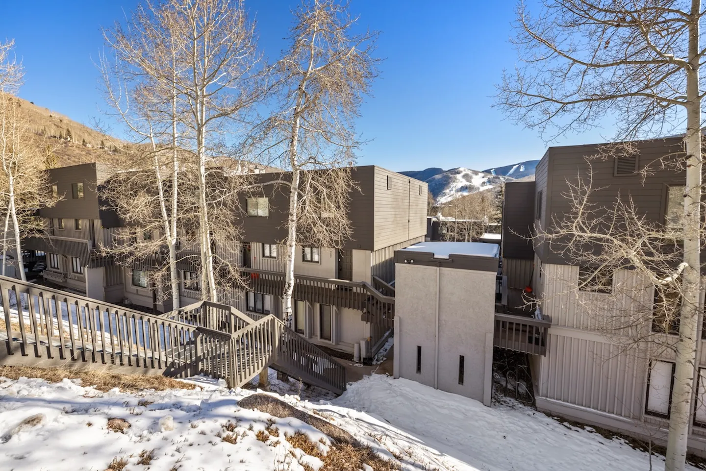 Exterior view of multi-story condominium buildings in a winter setting with snow and mountain views under a blue sky.