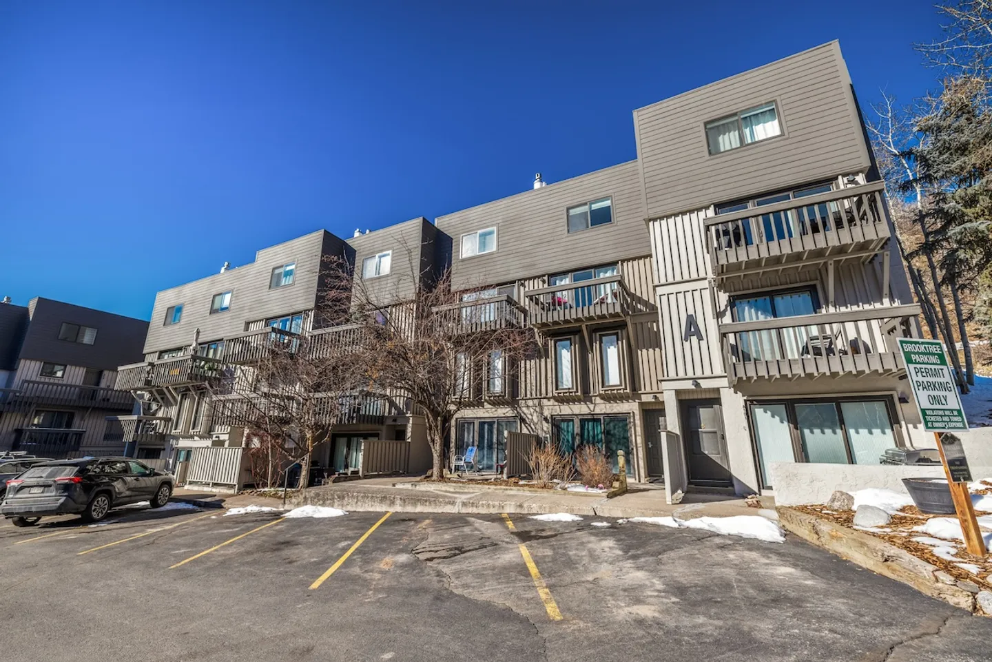 Exterior of a multi-story condo complex with wooden balconies and a paved parking lot under a clear blue sky.