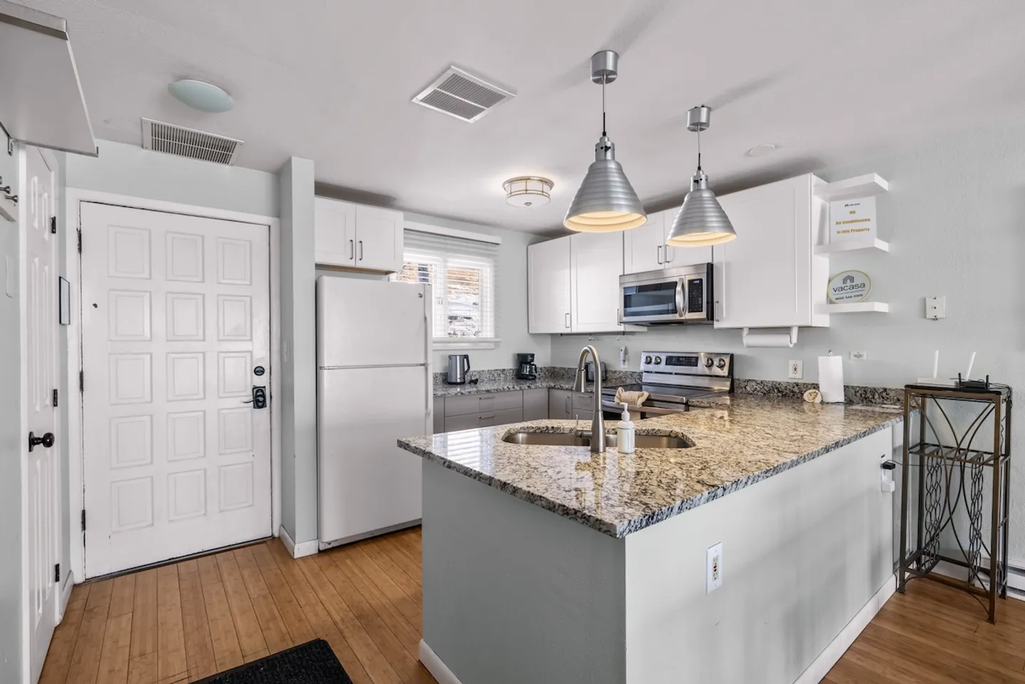 Kitchen with granite-look countertops, an island with an integrated sink, white upper cabinets, and white appliances.