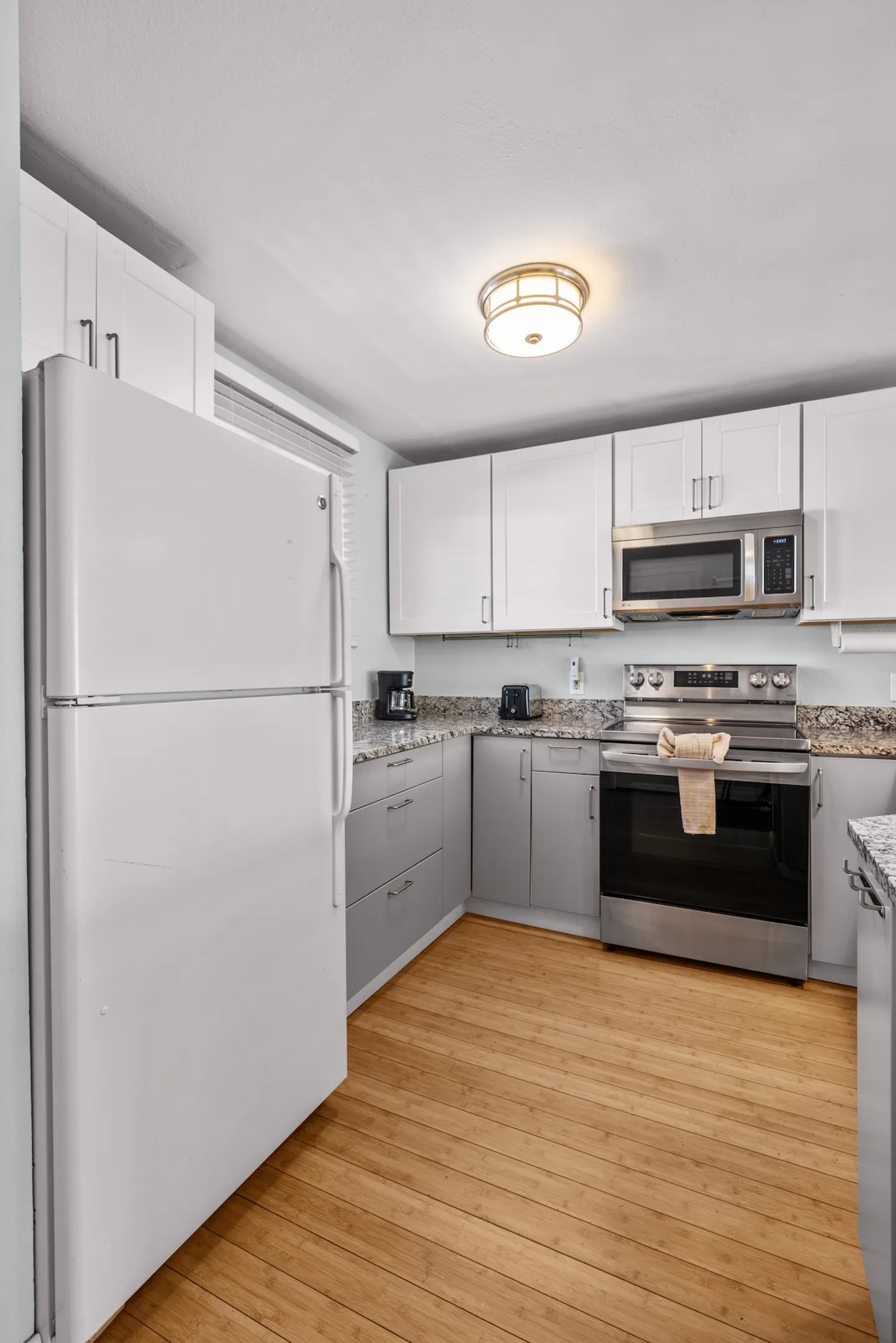 Kitchen featuring two-tone white and gray cabinets, speckled countertops, stainless steel stove, microwave, and a white refrigerator over light wood flooring.