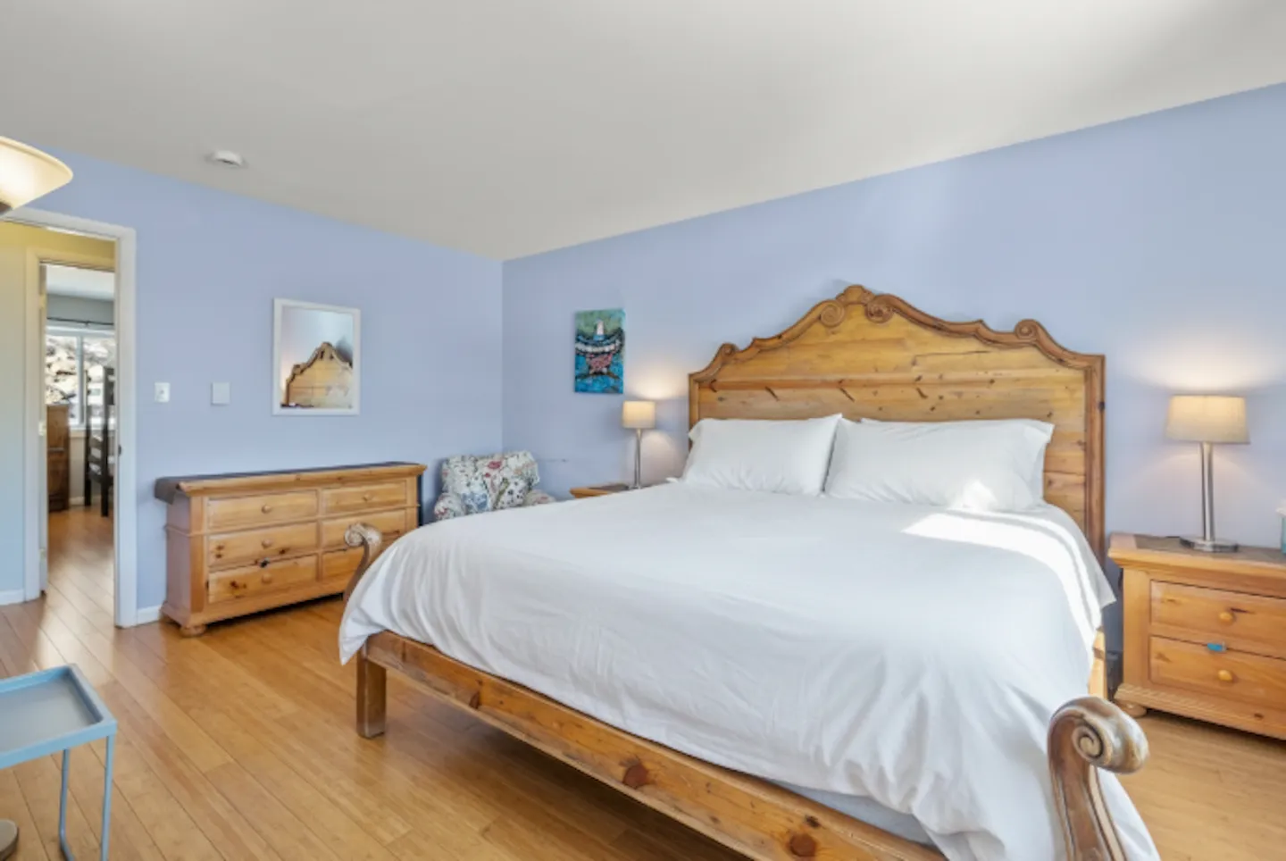 Bedroom with blue walls, light wood flooring, a wooden bed frame with white bedding, matching nightstands, and a dresser.