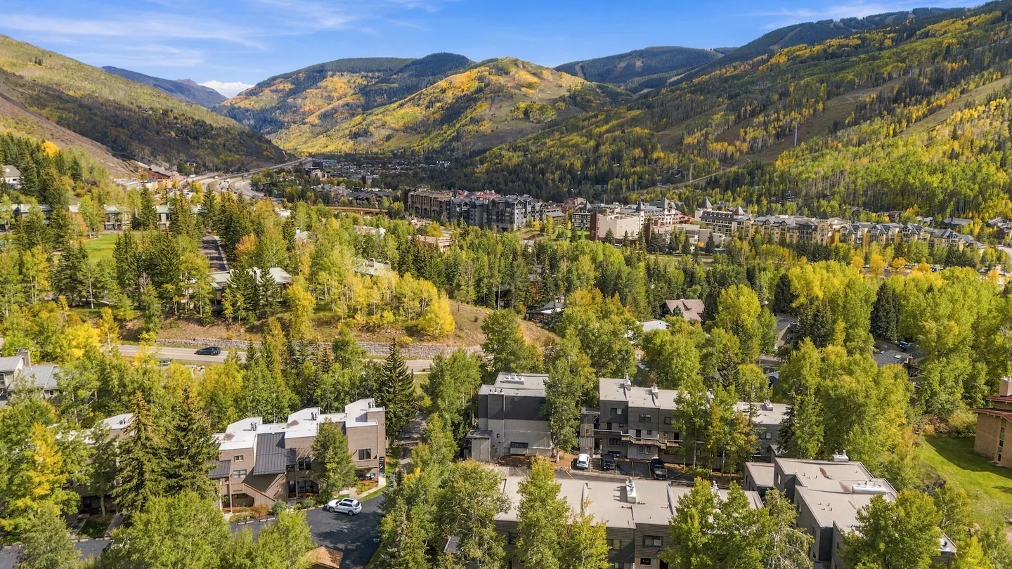 Aerial view of a mountain valley community with homes nestled among autumn trees and hills in the background.