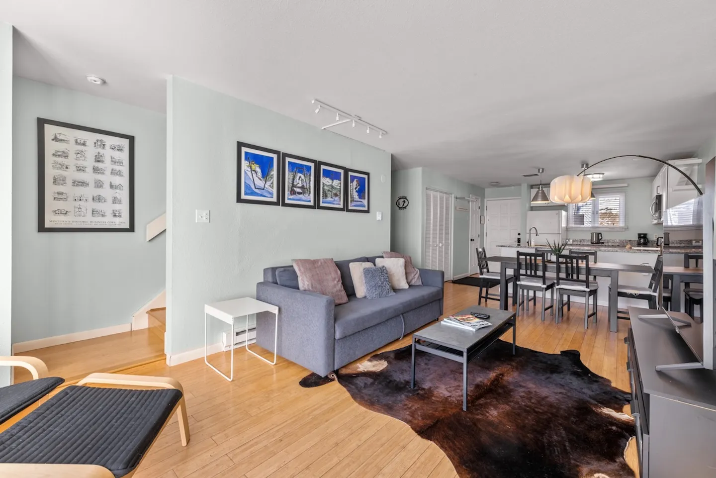 Open-concept living room with a blue couch, faux fur rug, and view toward the dining area and kitchen.