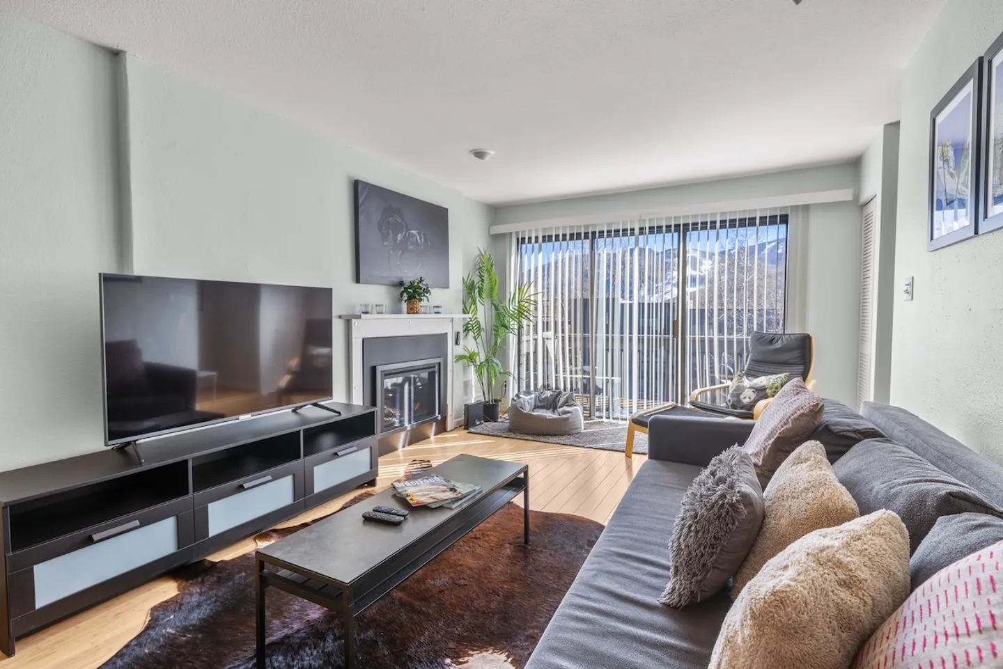 Living room with a sofa, coffee table, TV on a media console, fireplace, and sliding glass doors leading to a balcony.