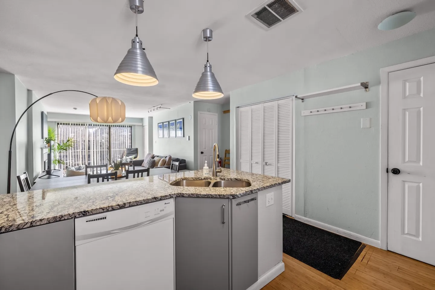 Kitchen island with a sink and dishwasher overlooking an open-plan dining and living area.