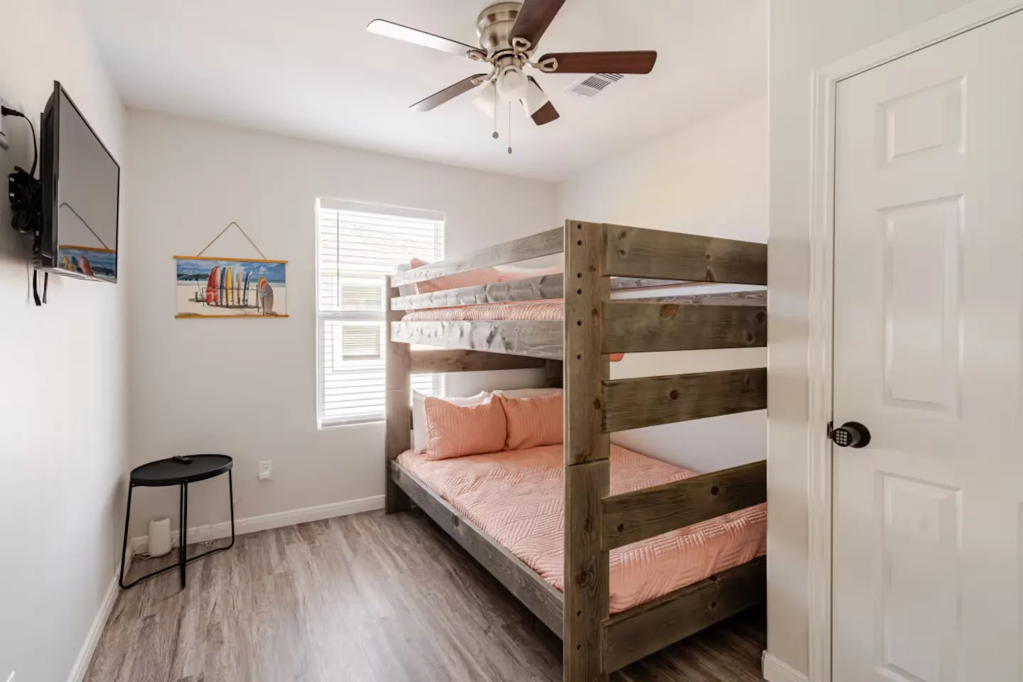 Bedroom featuring a wooden bunk bed with pink bedding, a wall-mounted TV, a ceiling fan, and wood-look flooring.