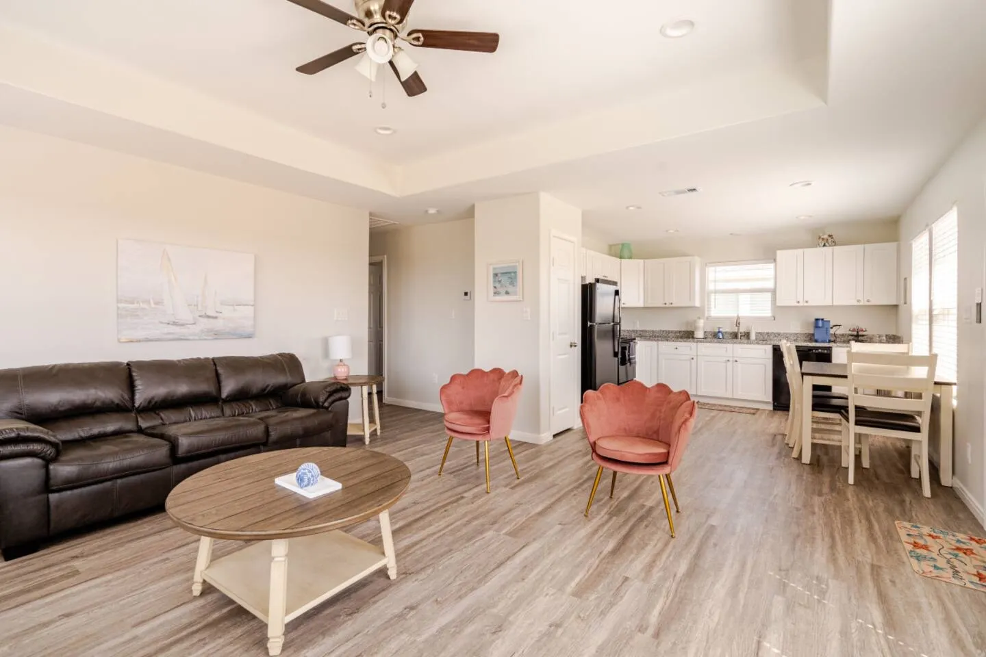 Open-concept living room with a brown leather sofa, pink accent chairs, and an adjoining kitchen and dining area.