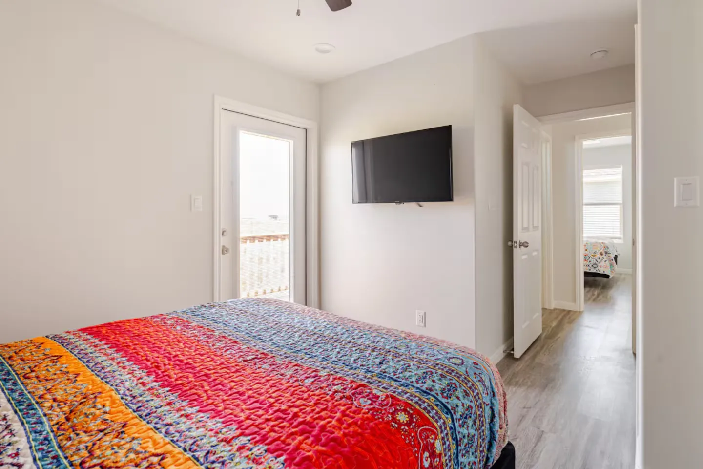 Bedroom featuring a colorful patterned bedspread, wall-mounted television, and glass door leading to an outdoor deck.