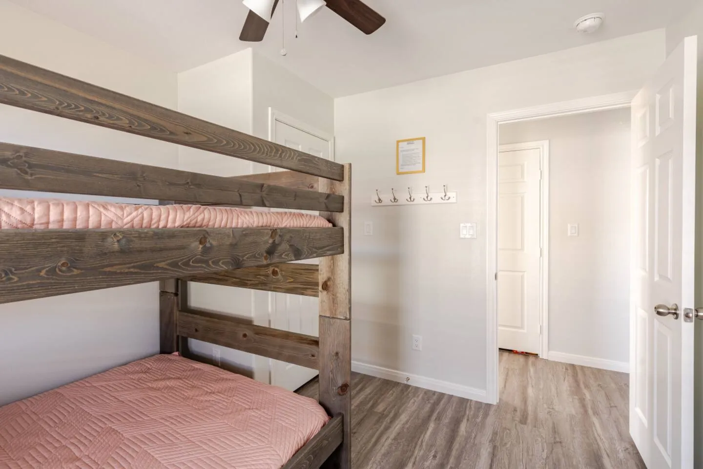 Bedroom featuring rustic wooden bunk beds with pink quilted bedding and an open doorway leading to a hallway.