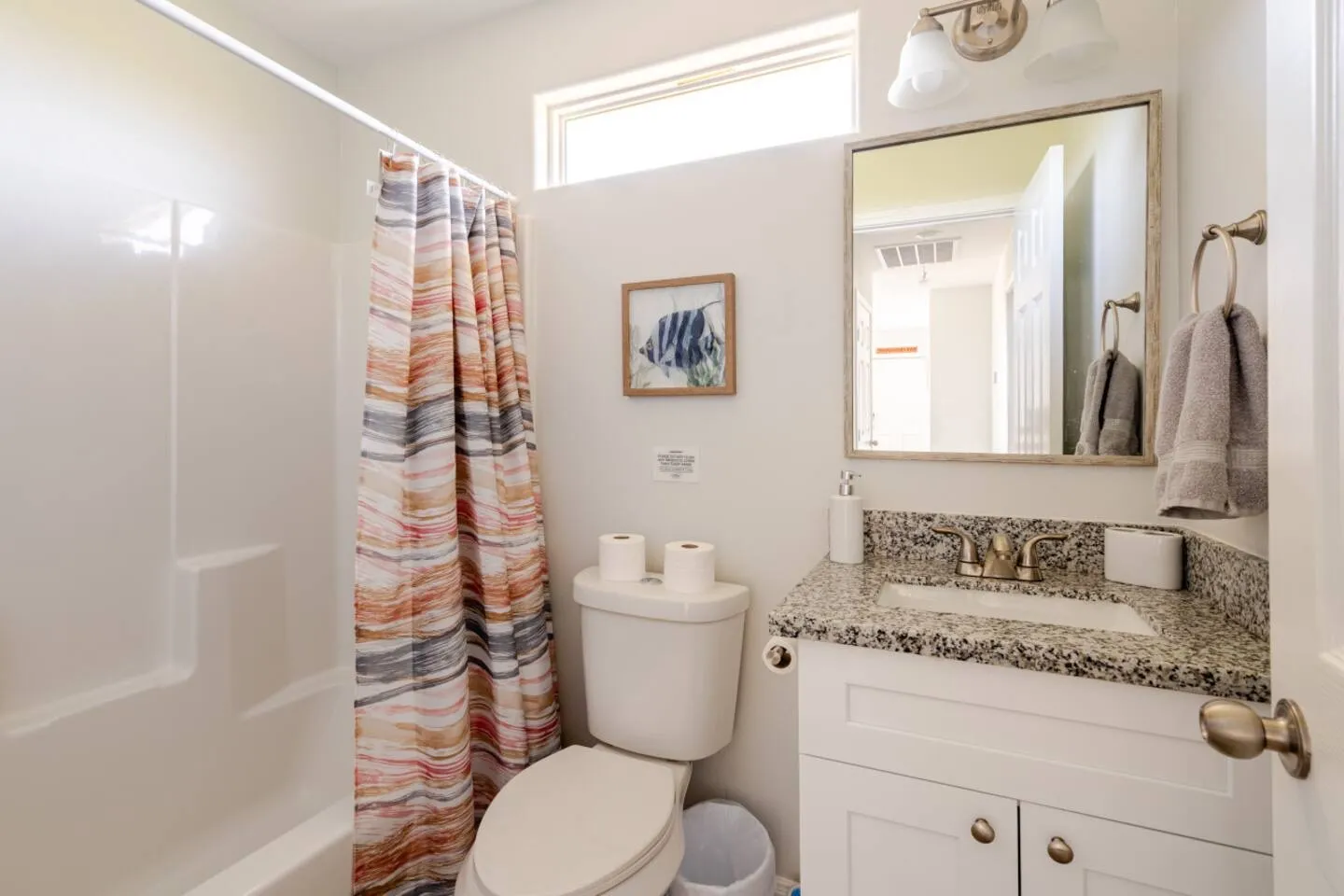Bathroom with a white vanity with granite countertop, toilet, and shower-tub combination with a patterned curtain.
