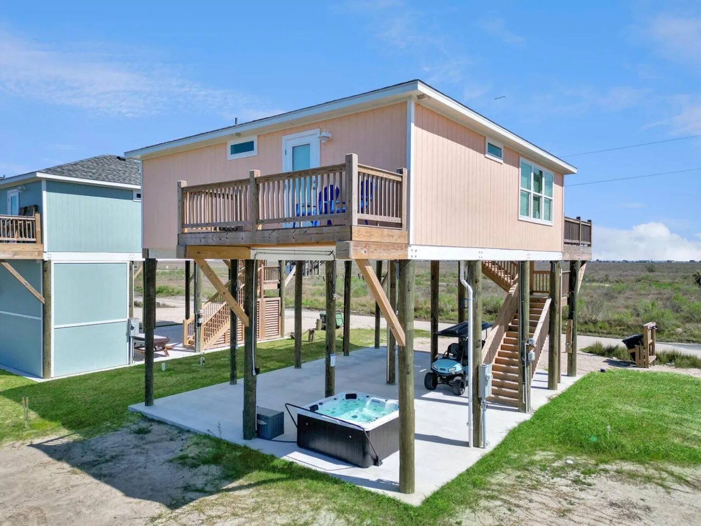 Exterior of an elevated stilt house with a hot tub and golf cart on the concrete ground level below.