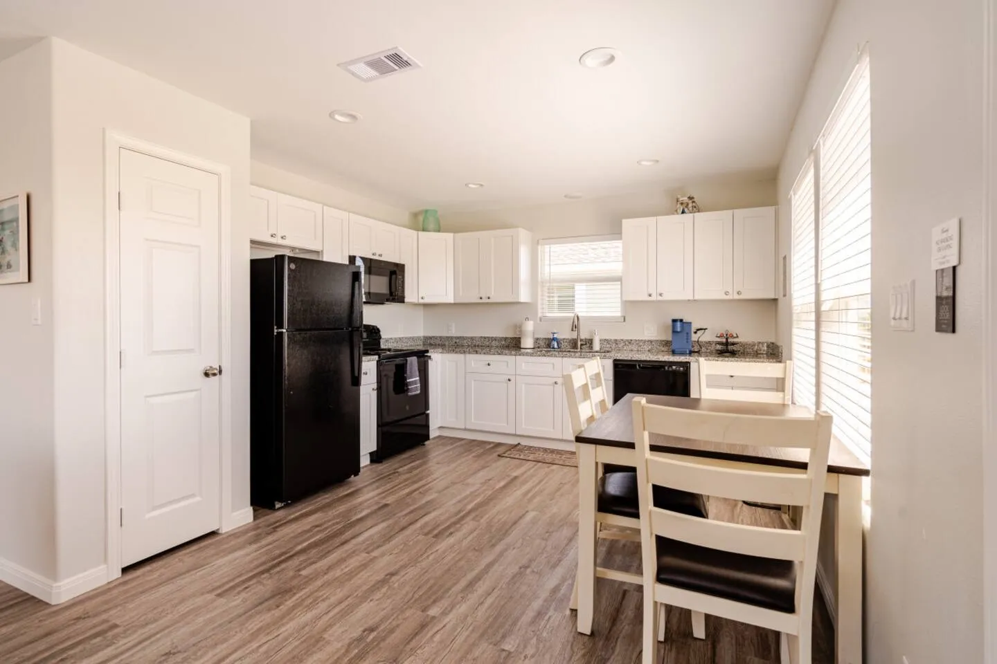 Kitchen and dining area with white cabinets, dark appliances, wood-look flooring, and a small dining table with chairs.