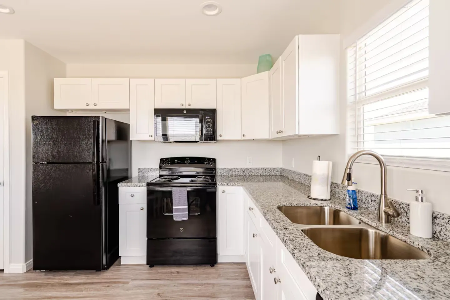 Bright kitchen with white cabinetry, speckled granite-look countertops, and black appliances.