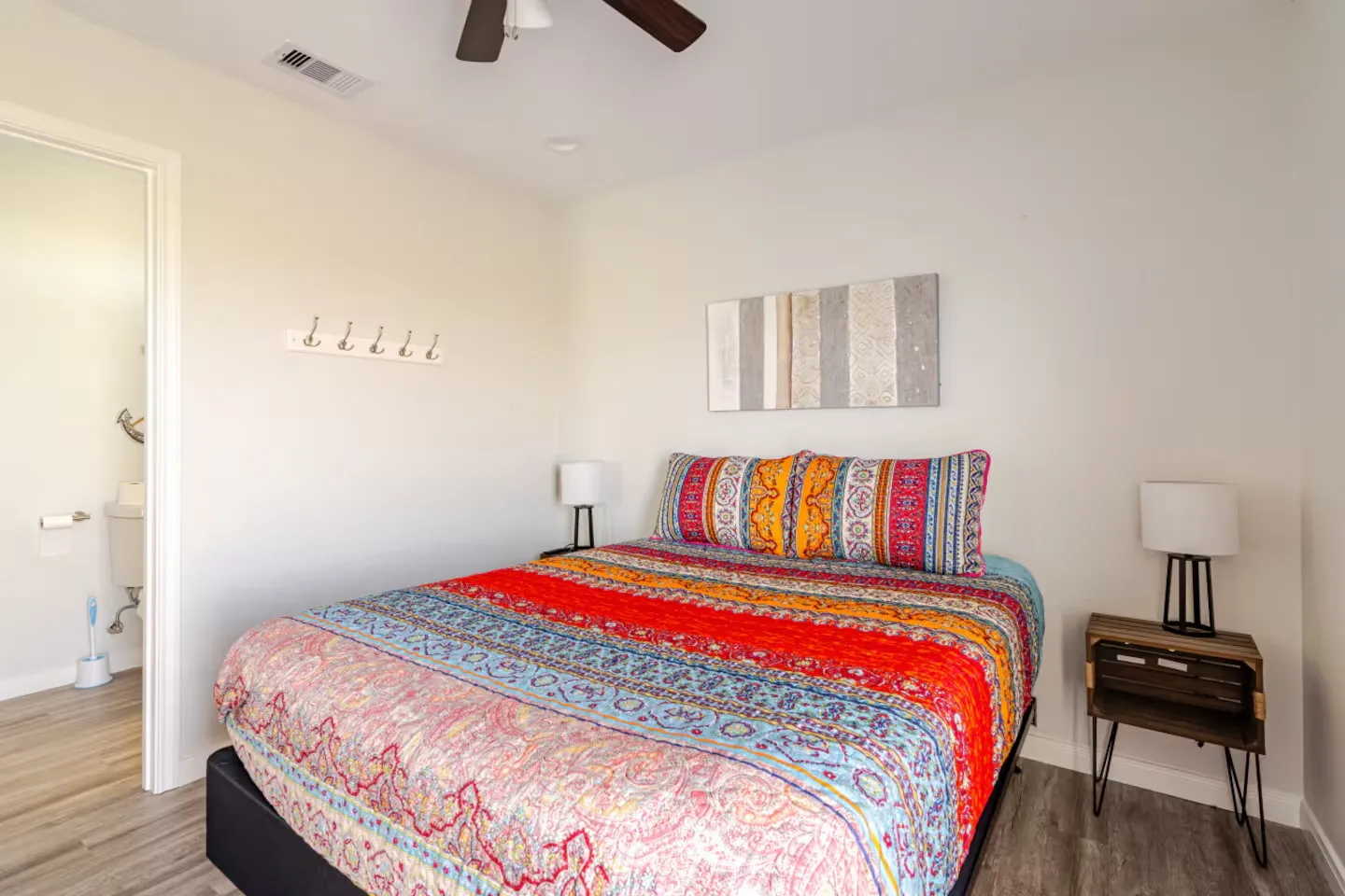 Bedroom featuring a bed with a colorful patterned quilt, bedside tables with lamps, and an open doorway to an adjoining bathroom.