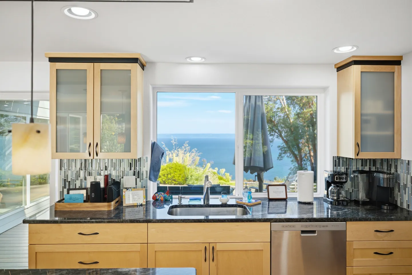 Kitchen sink and counter with light wood cabinets and a window overlooking the ocean.