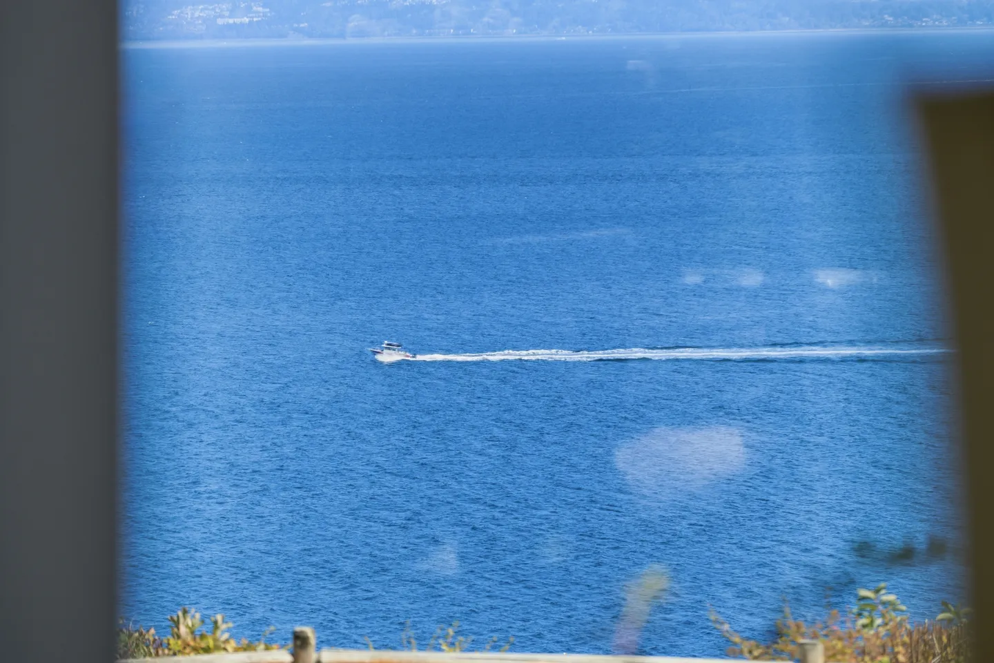 View of a boat leaving a wake on open blue water seen past vegetation and architectural framing.