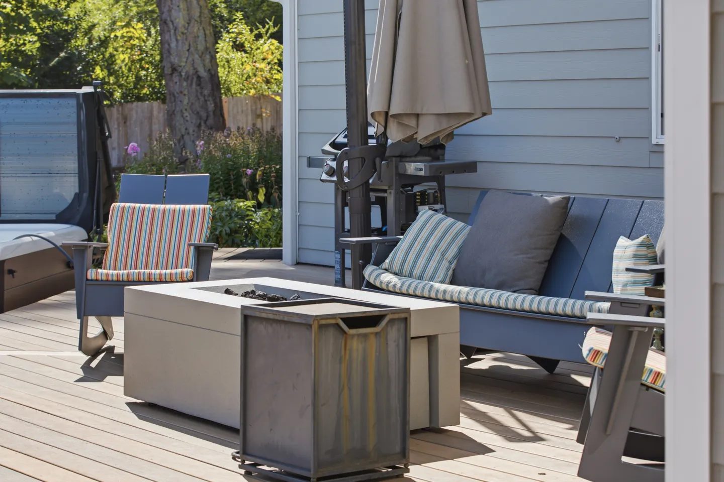 Outdoor deck featuring a fire pit table, outdoor seating with cushions, a hot tub, and a barbecue grill against gray siding.