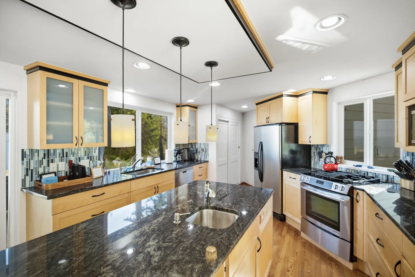 Kitchen with light wood cabinetry, dark patterned countertops, stainless steel appliances, and a central island with a small sink.