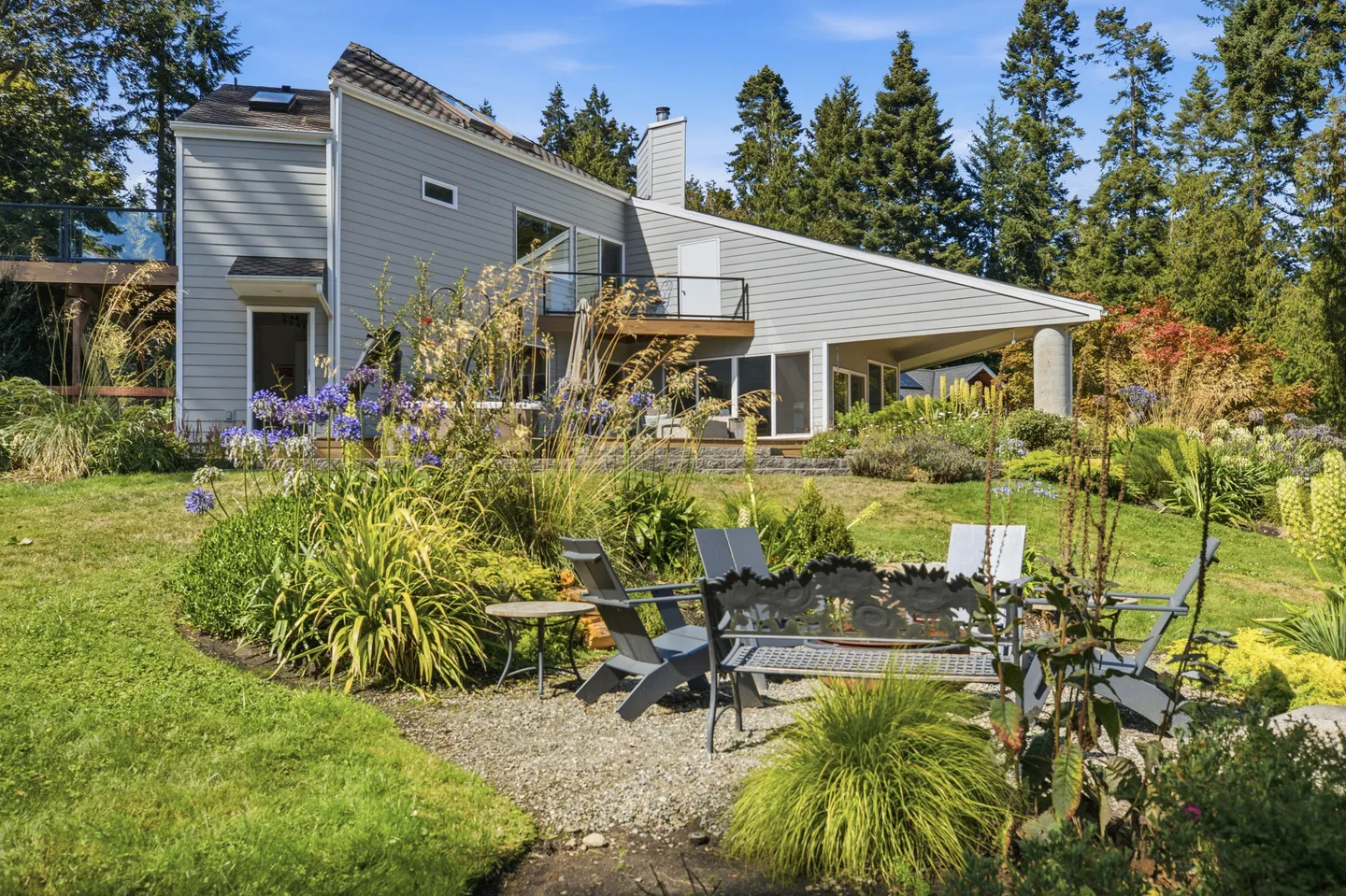 Rear exterior view of a multi-level contemporary home with a landscaped yard and a gravel seating area.